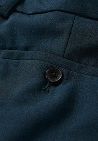 Tissu bleu marine à la texture lisse, avec un bouton noir orné d'un détail en fil et une couture de poche.