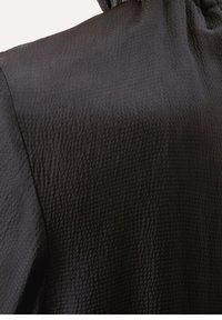 Czarna tkanina o fakturze z lekko pomarszczoną powierzchnią. Ubranie ma marszczony dekolt, podkreślający miękki przepływ i kształt.