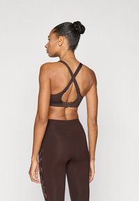 Hnedá športová podprsenka s krížovými ramienkami, nastaviteľnými háčikmi a výrezom na chrbte. Dopĺňa ju pár zladených legín s vysokým pásom.