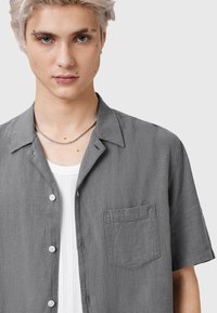 Grijze kortemou shirt van textuurstof, met een casual kraag en een borstzak met knoopsluiting aan de voorkant.