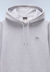 Sudadera gris con capucha, hecha de un tejido suave. Presenta un logo en el pecho y cordones blancos que atraviesan la capucha.