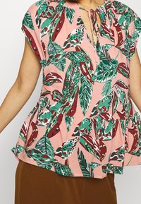 Top peplum floreale rosa, con motivi di foglie verdi e bordeaux, scollo rotondo con dettaglio a fiocco e maniche corte. Realizzato in un tessuto leggero.