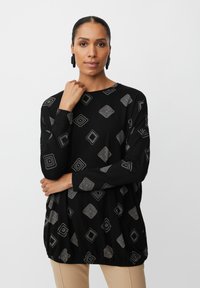 Schwarzes Langarmoberteil mit einem geometrischen silbernen Muster, mit einem gerafften Saum und weichem Textilstoff. Geeignet für die Freizeit.