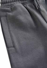 Grijze sportieve joggers gemaakt van zachte stof, met een elastische tailleband, een trekkoord en een zijzak met een gladde textuur.