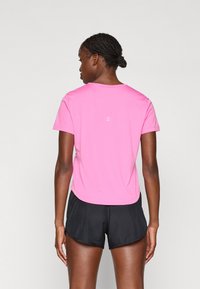Kortermet rosa treningsskjorte med rund hals. Glatt stoff, har et minimalistisk design og inkluderer en subtil logo på baksiden.