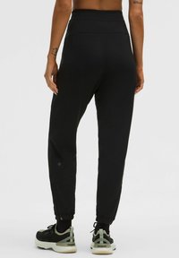 Juodos sportinės kelnes su aukšta juosta, siaurėjančiomis kojomis ir užtrauktukais ant kulkšnies. Lygi tekstūra, sukurta patogumui ir lankstumui.