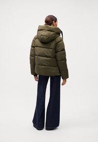 Giacca a vento verde oliva con cappuccio, caratterizzata da un design trapuntato e una vestibilità rilassata. Abbinata a pantaloni in denim scuri a gamba larga.