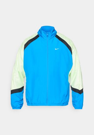 Blue Nike jacket with a high collar, mesh green panels, black accents on shoulders and cuffs, and a full front zipper. Features elastic cuffs.
