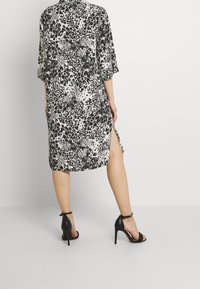 Robe en imprimé léopard en tissu léger avec des manches courtes et des fentes sur les côtés, associée à des sandales à talons hauts noires.