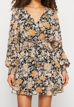 Blomstret V-hals kjole med lange gennemsigtige ærmer, indsnøret talje og sort baggrund med beige og hvide blomster.