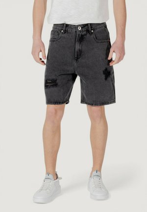Shorts in denim nero con dettagli strappati, cinque tasche e una vita con chiusura a bottone, abbinati a sneakers bianche.