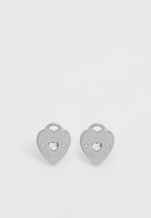 Ezüst szív alakú fülbevalók, amelyekbe az "GUESS AMORE" felirat van gravírozva, középen egy szív alakú kővel és mindkét oldalon két tiszta kiegészítővel.
