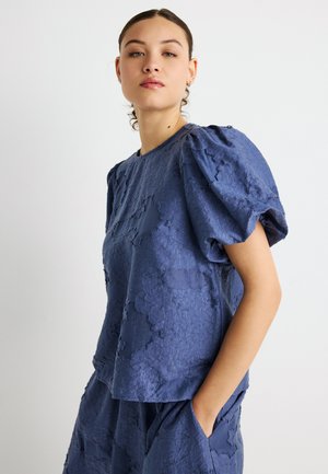 Blå tekstureret top med puffede ærmer og blomsterprint. Rund halsudskæring og afslappet pasform, kombineret med matchende underdele.