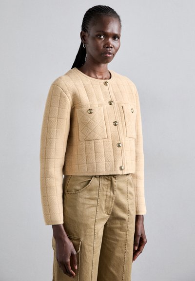 Μπεζ καπιτονέ τζάκετ με χρυσά κουμπιά, δύο τσέπες με πατσαβούρα και cropped σχέδιο. Το ύφασμα από μείγμα βαμβακιού προσφέρει υφή.