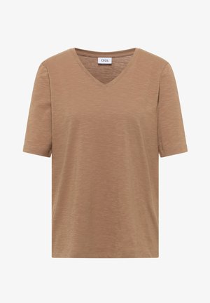 Femme aux cheveux courts bruns portant un t-shirt marron uni à manches courtes et un jean denim bleu clair, dos à la caméra.