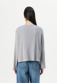 Gray, ribbed long-sleeve top with a round neckline and a cropped hem, paired with high-waisted blue denim jeans. Simple, textured design.