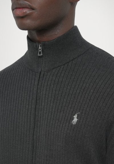 Szürke bordázott, cipzáros pulóver magas gallérral, bal oldalon kis hímzett logóval és sima textúrával.