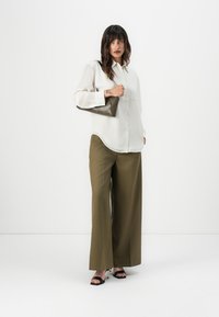 White long-sleeve shirt with a relaxed fit, olive green wide-leg trousers, and a dark brown clutch bag. Black strappy heels complete the look.
