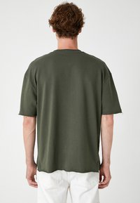 Olivengrøn oversized t-shirt med korte ærmer, rå kantbehandling og rund halsudskæring. Lavet af blødt stof, enkel og afslappet pasform.