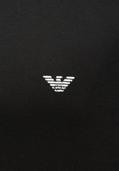 Λευκό στυλιζαρισμένο λογότυπο αετού στο κέντρο σε μαύρο υφασμάτινο φόντο, με οριζόντιες γραμμές που σχηματίζουν τα φτερά και το σώμα.