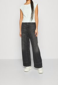 Svetle modrý pruhovaný crop top s krátkými rukávy, kombinovaný s širokými vybledlými černými džíny. Nosené s bílými teniskami. Jednoduchý design.