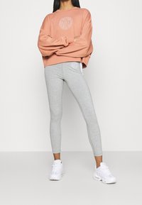 Light pink sweatshirt with a round logo, paired with light grey leggings featuring a logo, worn with white athletic sneakers.