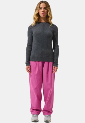 Maglione grigio a coste abbinato a pantaloni rosa larghi e sneakers grigie. Il maglione ha un design aderente e i pantaloni presentano una finitura testurizzata.