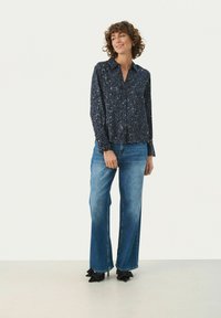 Mørkeblå skjorte med leopardmønster, lange ærmer og krave, parret med lyseblå bredbenede jeans og sorte hæle.
