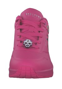 Rosa idrottssko med slät syntetisk ovandel, platta snören, dekorativt dödskalleaccent och strukturerad gummisul med rutmönster.