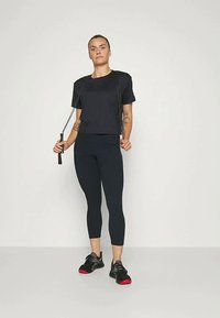 Must have lühikeste varrukatega sportlik topp, mustad retuusid ning punaste detailidega mustad spordijalatsid. Käes on hüppeköied.