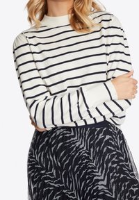 Randig stickad tröja i krämfärgad och marinblå, med hög hals och långa ärmar, tillsammans med en kjol med svart och grå zebramönster.