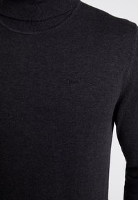 Mørkegrå rullekrave-trøje lavet af ribstrikket stof. Har et diskret prægede logo på brystet og tætsiddende lange ærmer.