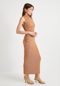 Hame midi coklat tanpa lengan yang pas badan dengan detail kerutan di samping. Dipadukan dengan sepatu hak tinggi metalik emas dengan tali. Tekstur yang halus.