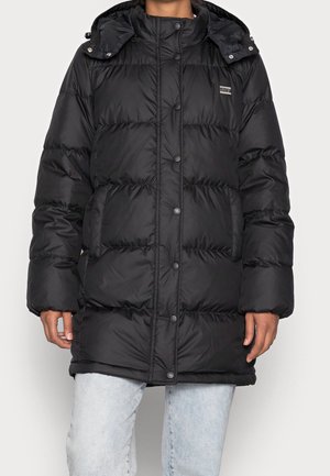 Personne portant une doudoune noire Levi's avec des boutons sur le devant, des poches latérales et une capuche, associée à un jean bleu clair.