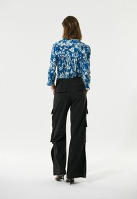 Langärmlige blaue Bluse mit Blumenmuster und gerafftem Rückendetail, kombiniert mit schwarzen, weiten Cargo-Hosen mit seitlichen Taschen und ausgestellten Säumen.