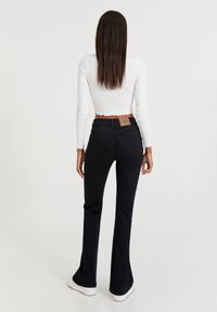 Jean noir évasé à taille haute, avec poches arrière et une étiquette en cuir marron. Associé à un haut blanc court à manches longues.