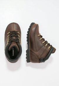 Brązowe skórzane buty trekkingowe z czarnymi akcentami, sznurówkami i złotymi oczkami. Posiadają solidną podeszwę dla lepszej przyczepności oraz wyściółkę dla komfortu.