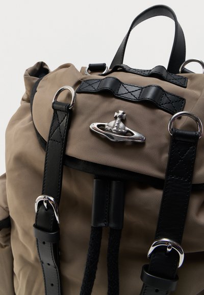 Μπεζ σακίδιο με μαύρα δερμάτινα λουριά, ασημένιες αγκράφες και ασημένιο έμβλημα σε σχήμα σφαίρας στο μπροστινό καπάκι.