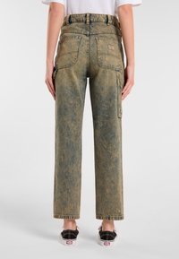 Pantaloni cargo in denim azzurro chiaro con finitura sbiadita, vita alta, gamba dritta, due tasche posteriori e cuciture a contrasto. Scarpe nere slip-on.