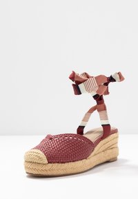 Rote gewebte Textil-Wedgesandale mit runder Zehenpartie, natürlichem Jute-Plateau und gemusterten Stoffbandagen am Knöchel in Streifen- und einfarbigen Varianten.