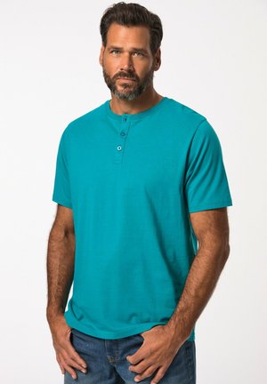 Camisa henley de manga corta en color azul verdoso con cuello redondo, tapeta de tres botones y textura de tela suave, combinada con jeans azules.