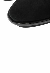 Zapatos de ante negro con un acabado suave, que presentan una punta redondeada y un borde texturizado a lo largo de la suela de goma.