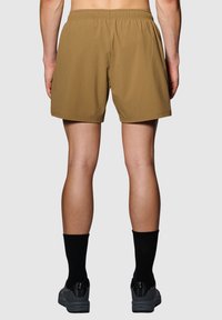 Kaki shorts met een elastische tailleband, een gladde textuur en een losse pasvorm. Draagt zwarte sokken en grijze schoenen. Alleen een achteraanzicht.