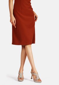 Sandali con tacco alto e cinturini elastici incrociati in un colore beige chiaro, caratterizzati da una superficie liscia e una design open toe.