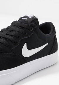 Černé skateboardové boty vyrobené z nubuku a plátna s bílým znakem Nike. Vybavené černými tkaničkami, polstrovaným jazykem a bílou gumovou podrážkou.