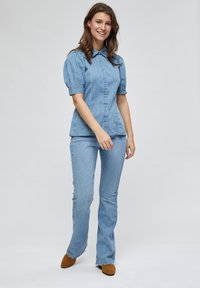 Top in denim azzurro con maniche a sbuffo e colletto, abbinato a jeans a palazzo coordinati. Le scarpe in camoscio marrone completano l'outfit.
