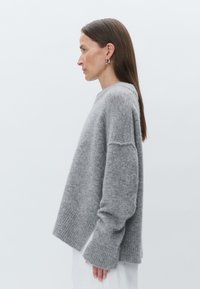 Suéter cinza de malha com um ajuste descontraído, punhos canelados e uma textura suave, exibido em um perfil lateral contra um fundo simples.