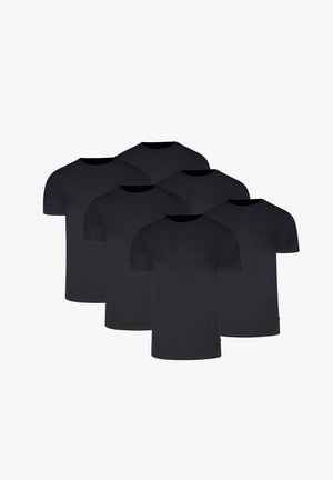 Mann trägt ein eng anliegendes schwarzes T-Shirt mit kurzen Ärmeln und hellgraue Boxershorts, steht vor einem einfarbigen hellen Hintergrund.