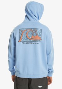 Light blue sweatshirt with a hood, featuring a graphic design on the back that includes a wave and mountain, labeled "Quiksilver."