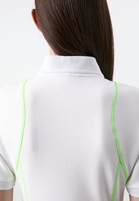 Polo bianco con tessuto testurizzato e dettagli in cucitura verde lungo le spalle e il colletto. Design semplice con un aspetto sportivo.